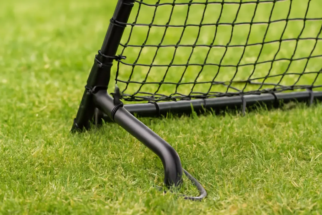 Editorial photograph of a close-up of an unbranded rebounder net frame joint and ground stake in grass