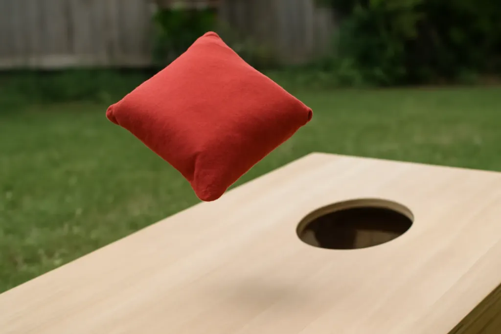 Editorial photograph of a close-up of an unbranded cornhole bag mid-air landing on a board outdoors